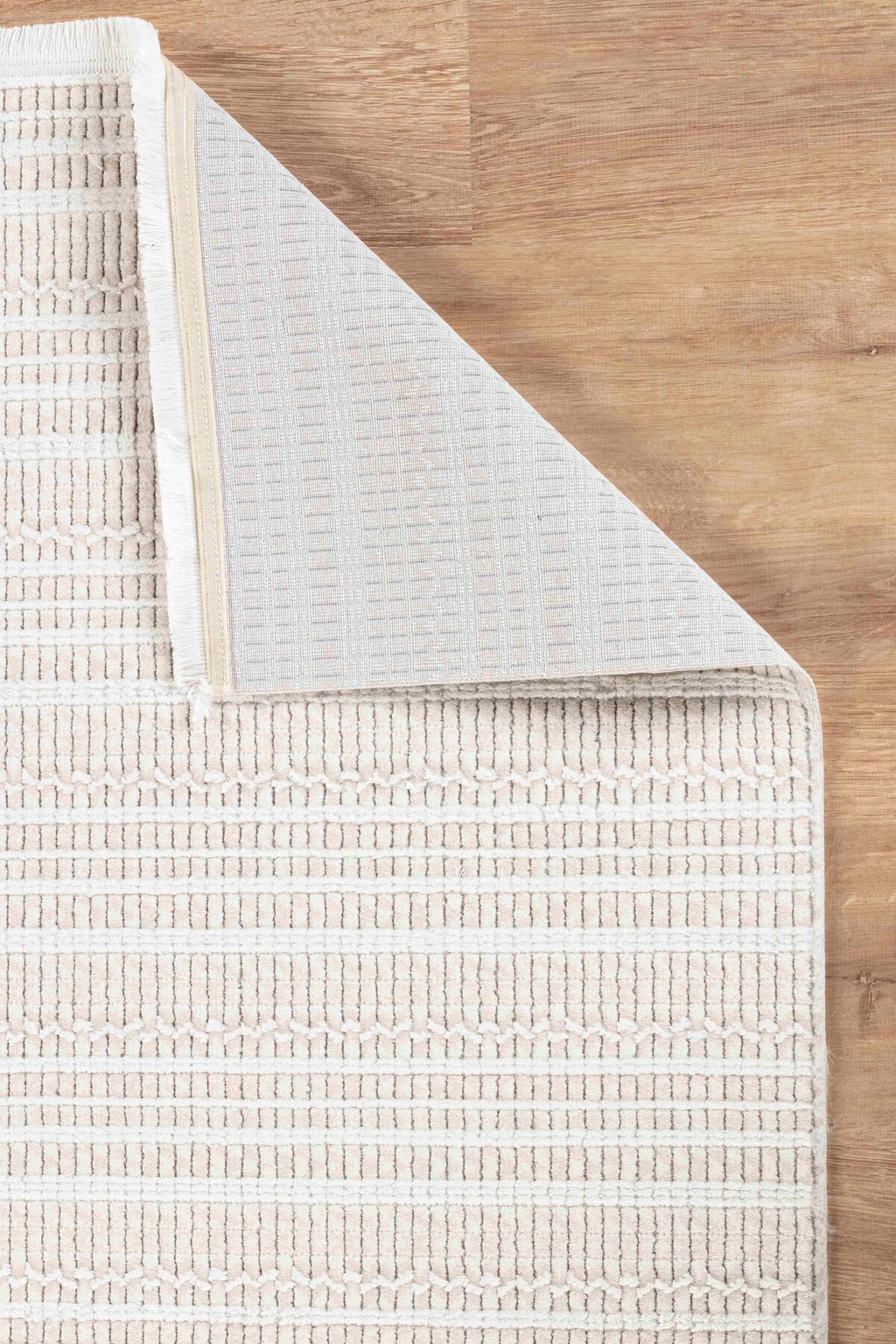 Açık renkli ahşap zemin üzerinde bej ve beyaz geometrik desenli yumuşak dokulu halı