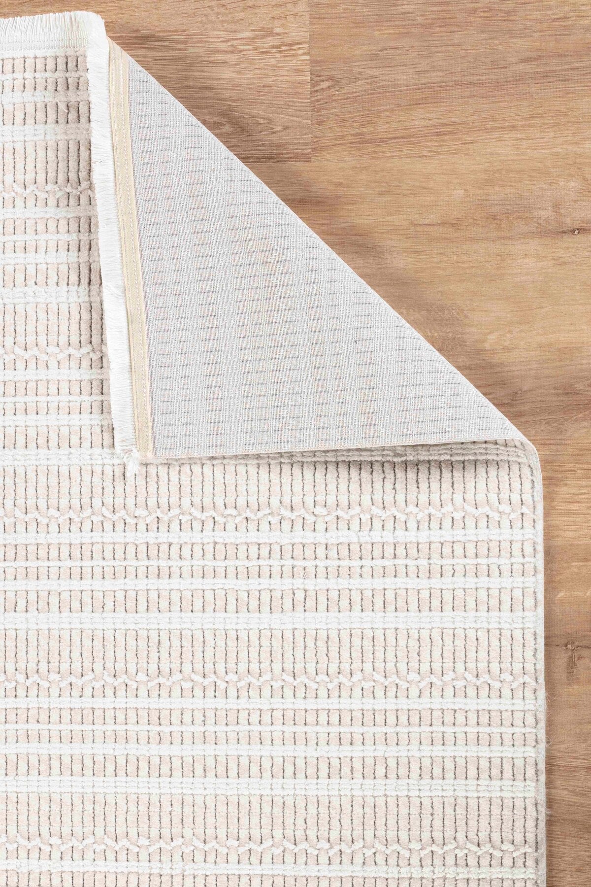 Açık renkli ahşap zemin üzerinde bej ve beyaz geometrik desenli yumuşak dokulu halı