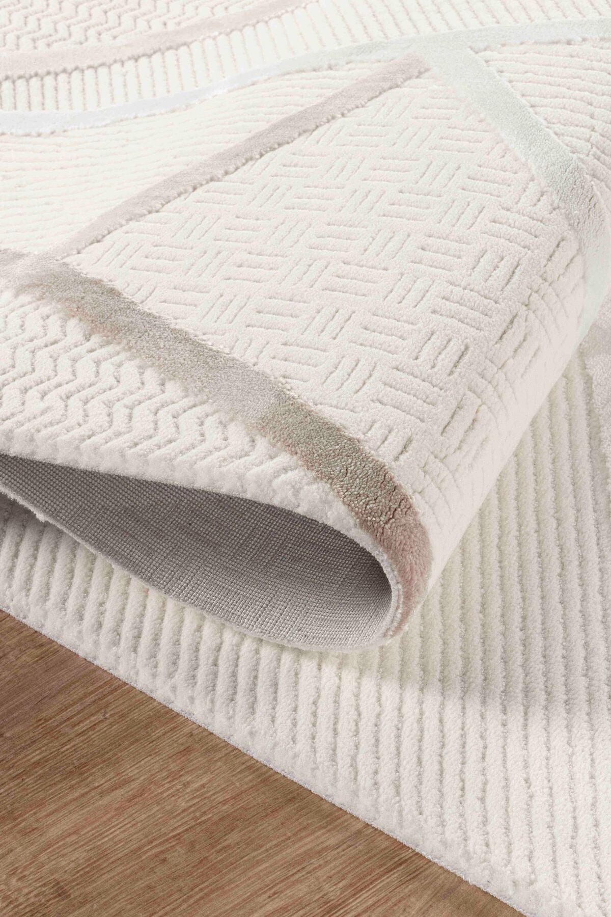 Desenli krem ve bej renkli yumuşak dokulu halı detayları, ahşap zeminde kıvrılmış halı ucu