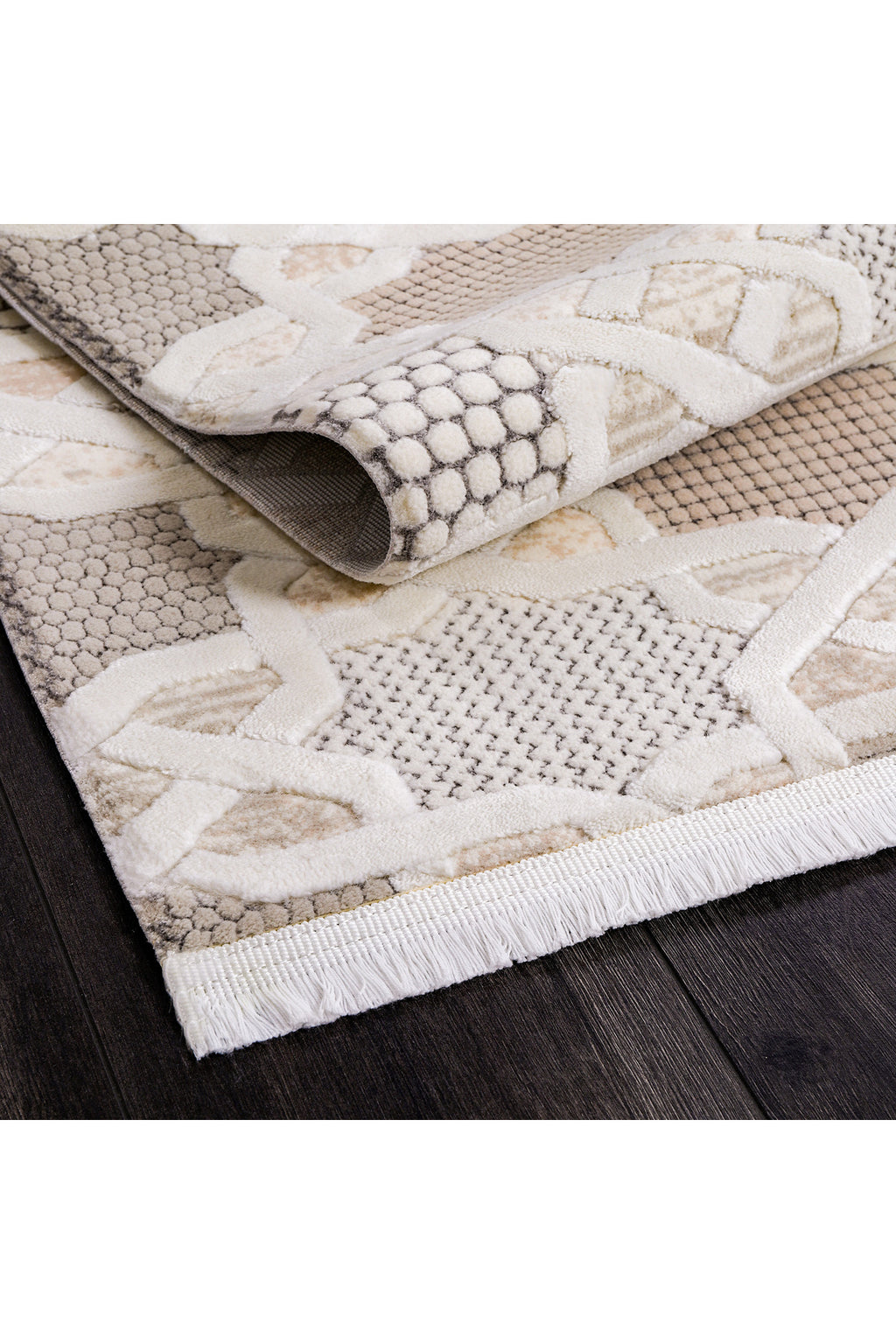 Koyu ahşap zemin üzerinde bej ve beyaz geometrik desenli kabartmalı halı ucu ve püskülleri