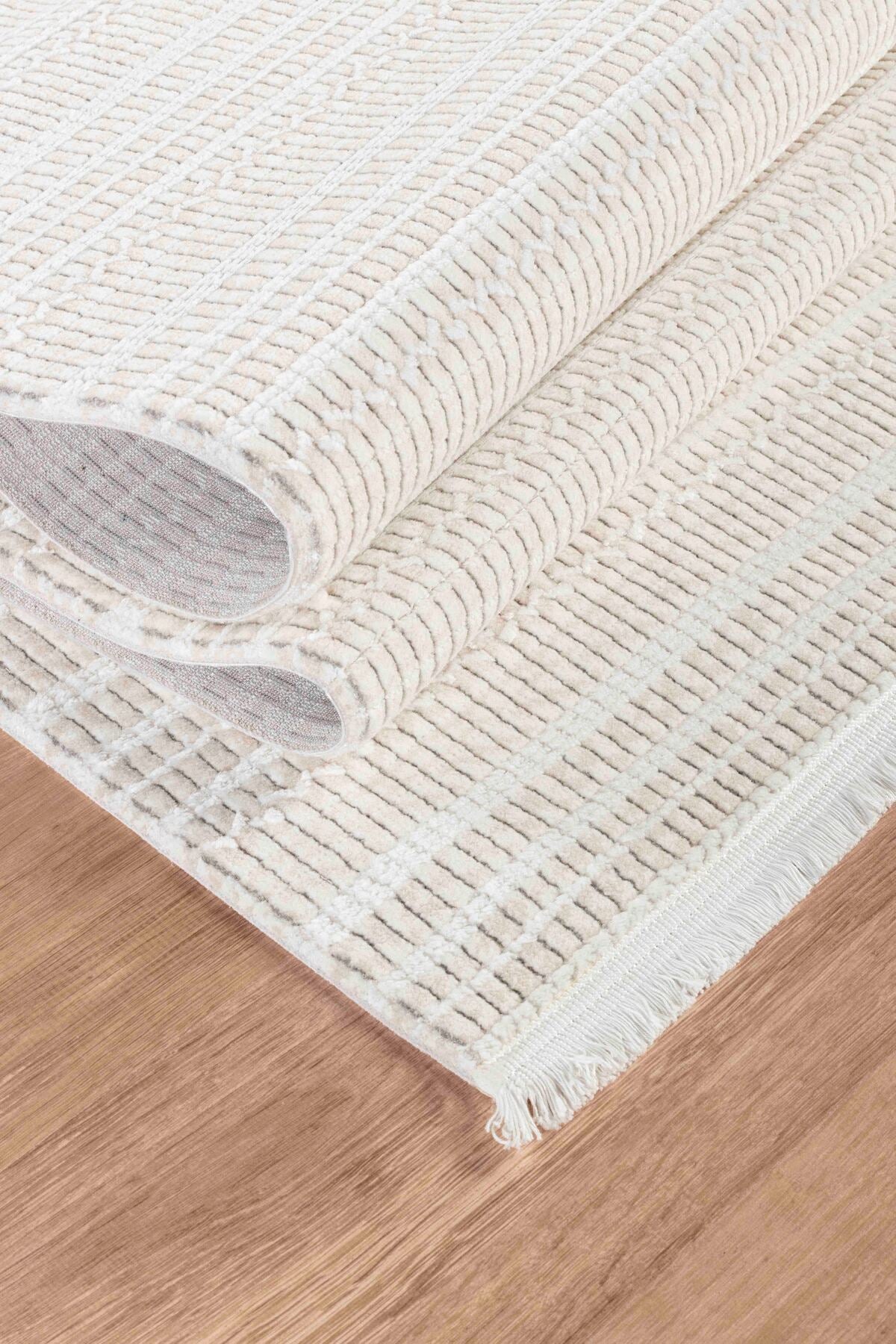 Krem ve beyaz çizgili dokulu yumuşak halı, ahşap zemin üzerinde kıvrılmış şekilde
