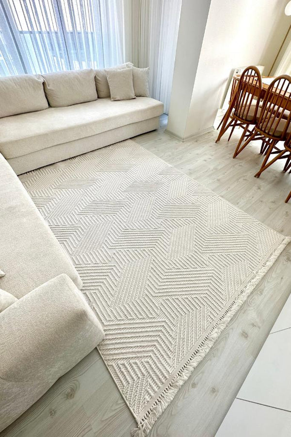 Açık renk modern oturma odasında krem renk L şekli kanepe ve geometrik desenli açık ton halı