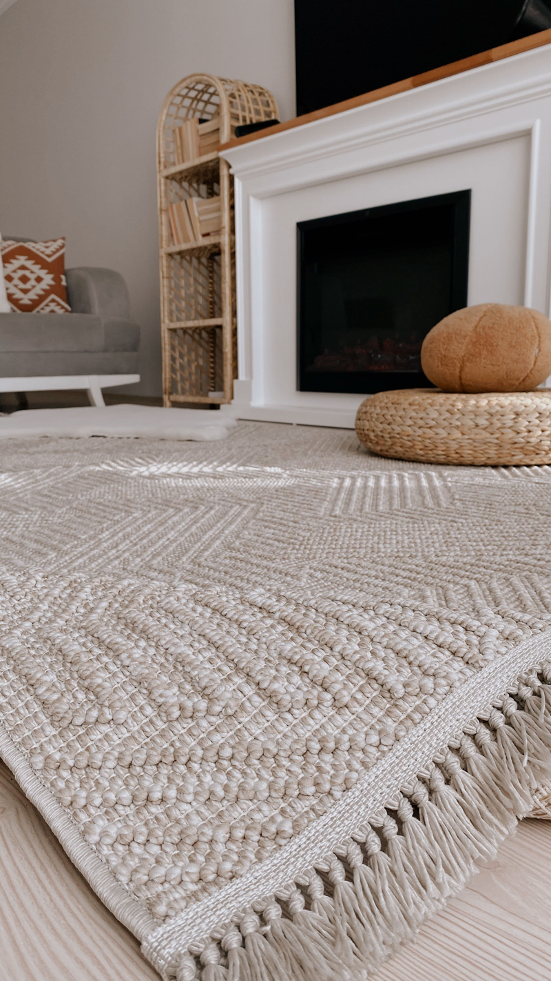 Doğal renklerde dokuma kilim, modern oturma odasında şömine ve hasır sepet ile