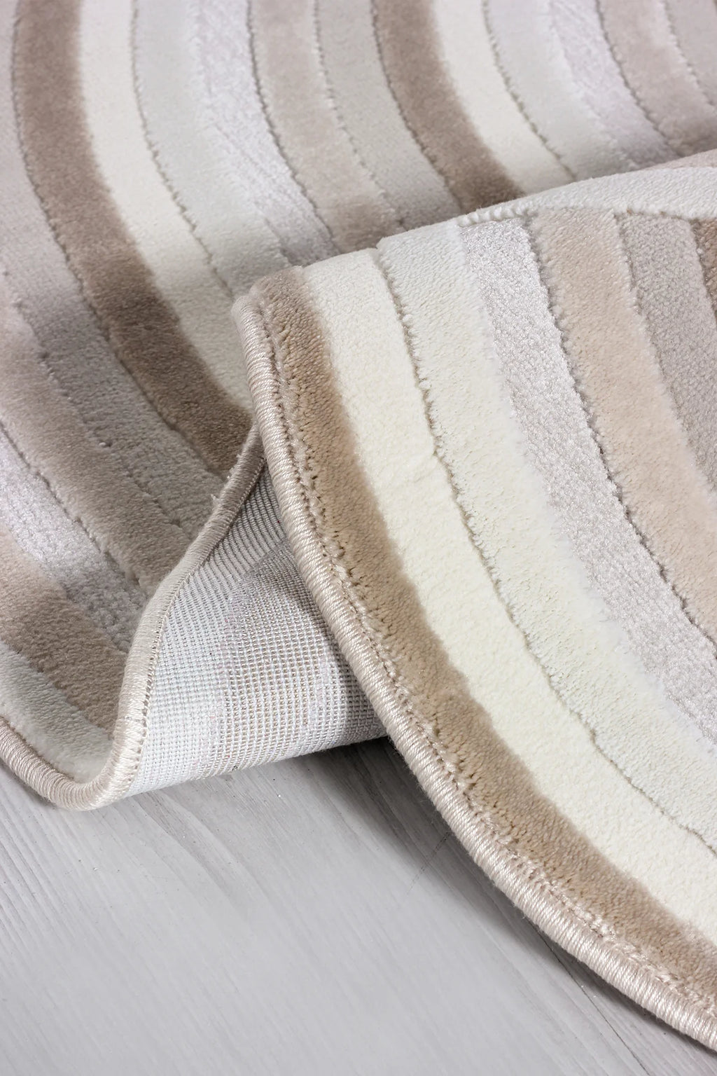 Krem ve bej tonlarında şerit desenli yumuşak dokulu makine halısı, açık zemin üzerinde