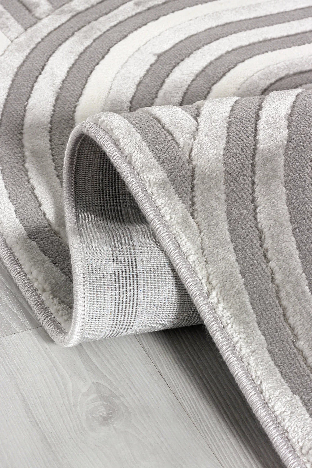 Krem ve gri renkli yumuşak dokulu desenli makine halısı, ahşap zeminde katlanmış