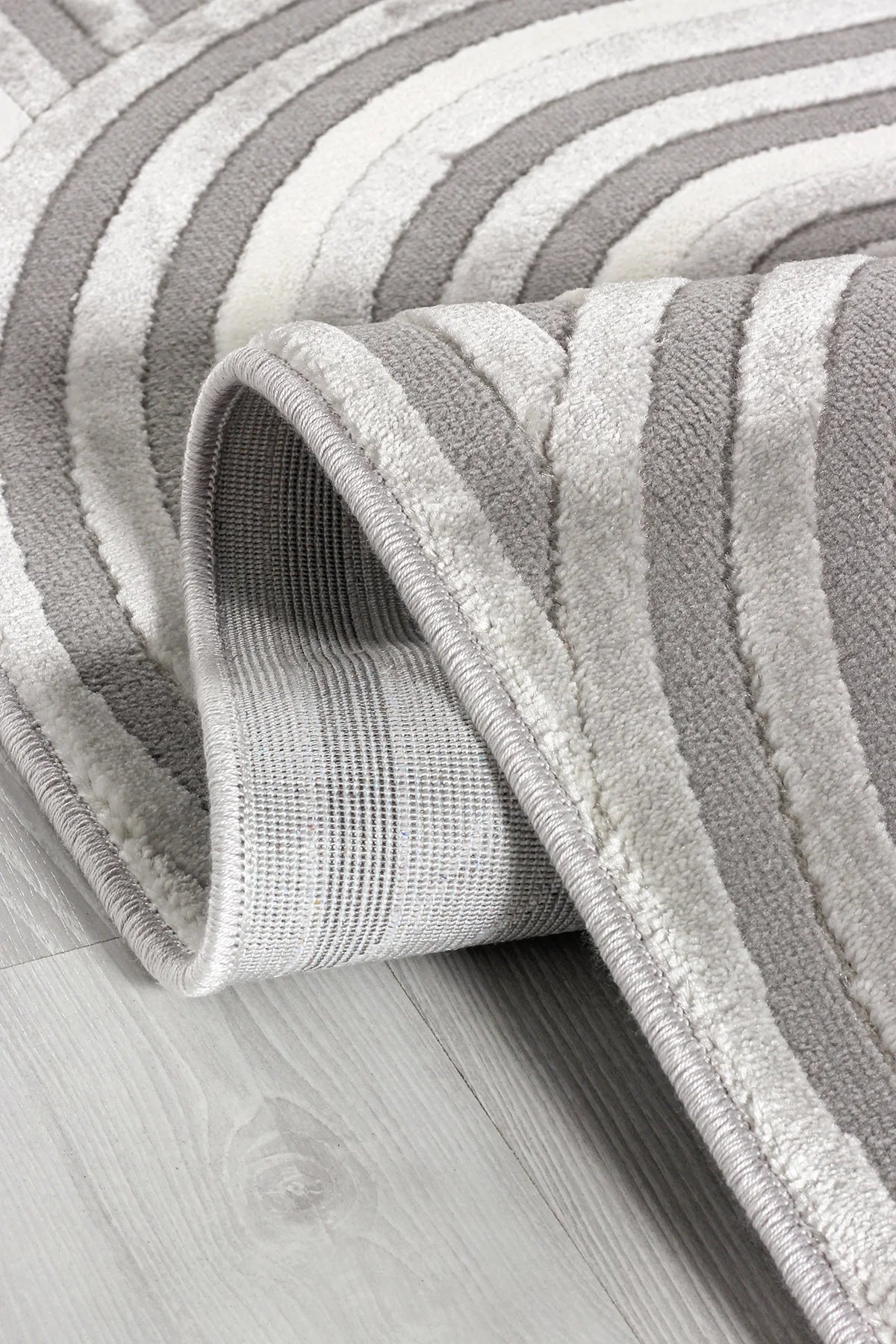 Krem ve gri renkli yumuşak dokulu desenli makine halısı, ahşap zeminde katlanmış