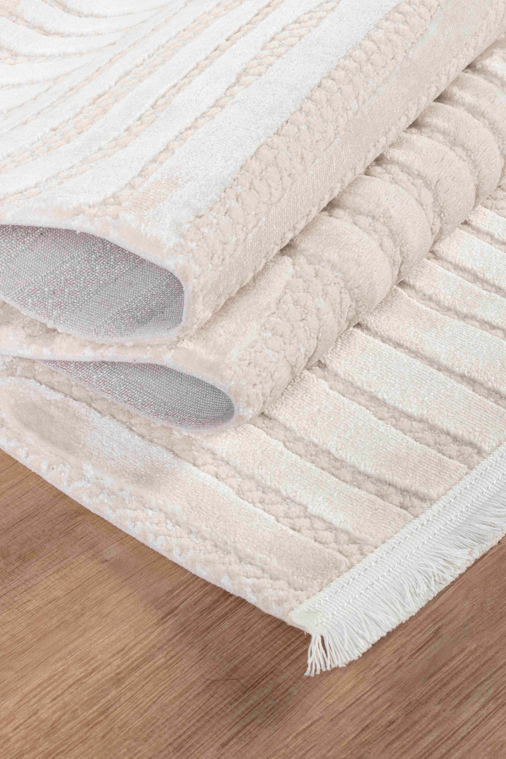Krem kahve yumuşak dokulu makine halısı, desenli ve kenarında beyaz püskül, ahşap zemin üstünde