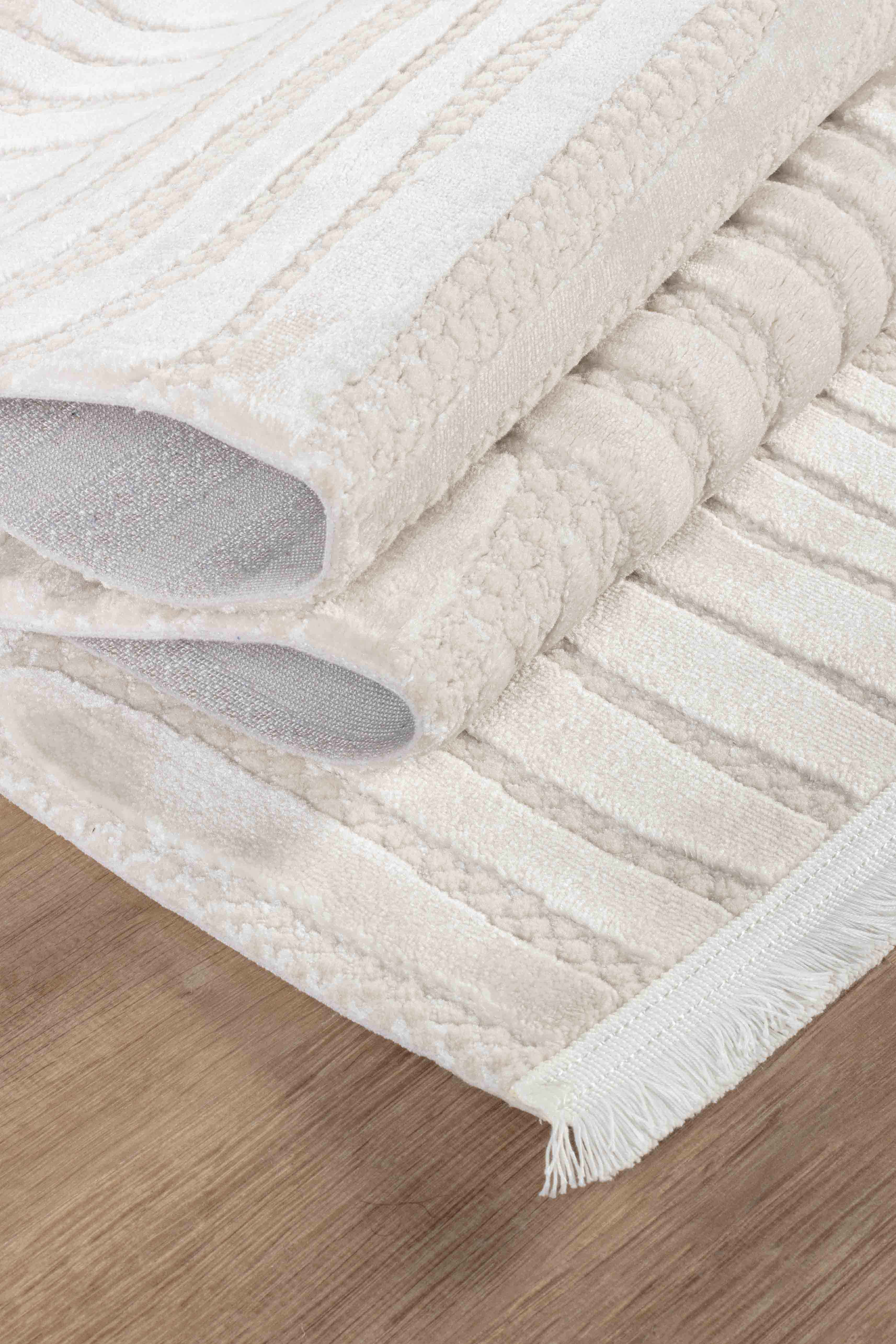 Krem kahve yumuşak dokulu makine halısı, desenli ve kenarında beyaz püskül, ahşap zemin üstünde