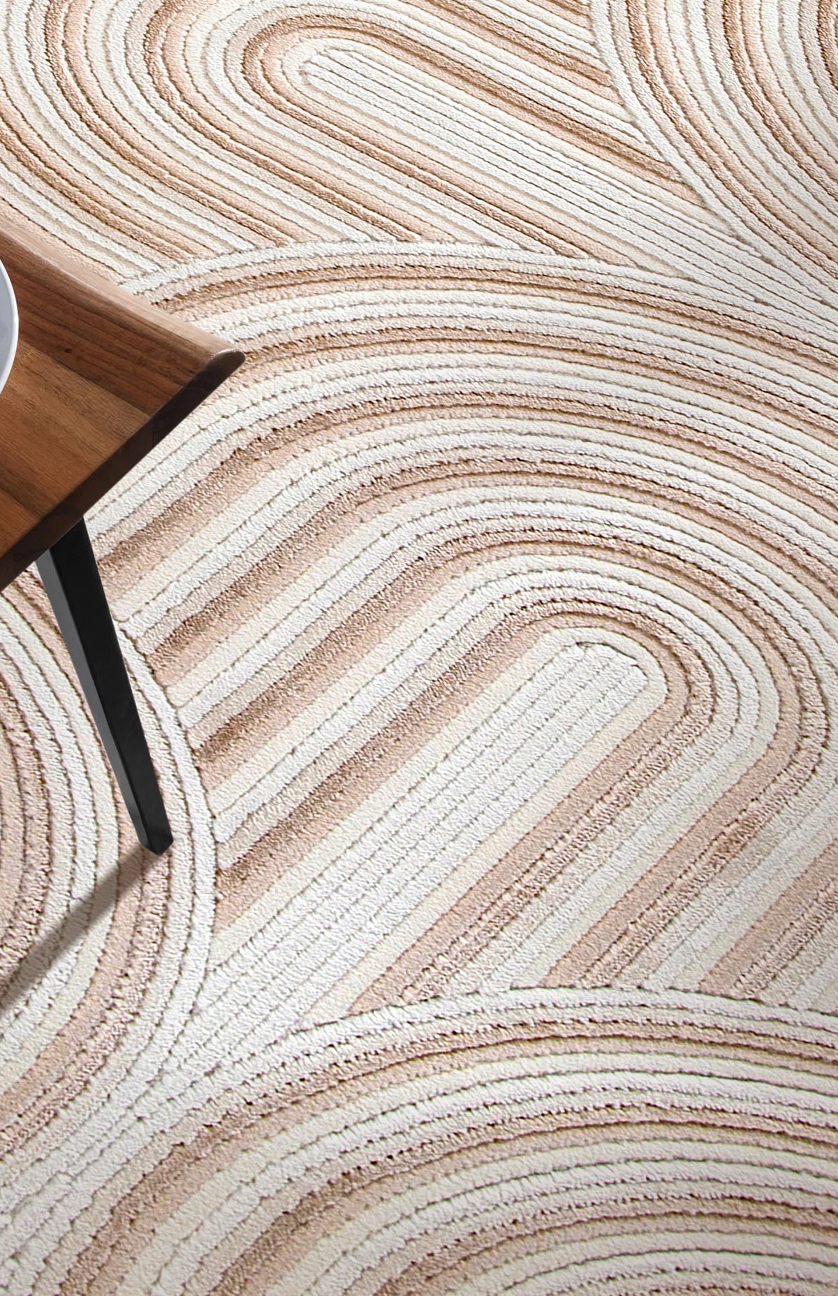 Bej ve krem renkli yuvarlak geometrik desenli yumuşak dokulu modern halı ve ahşap masa köşesi