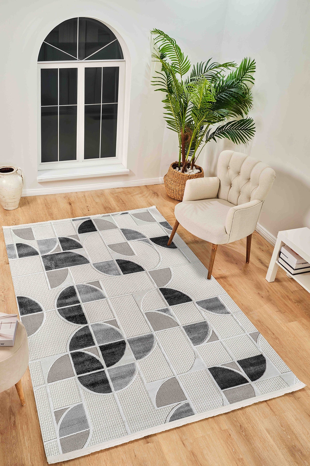 Gri ve siyah geometrik desenli modern yumuşak dokulu halı, beyaz berjer ve büyük salon bitkisi ile