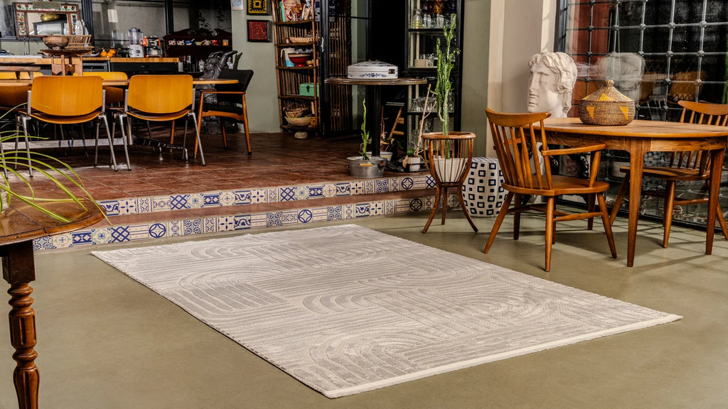 Beyaz desenli yumuşak dokulu salon halısı, ahşap masa ve sandalyeler, dekoratif bitkiler ve figür heykeli