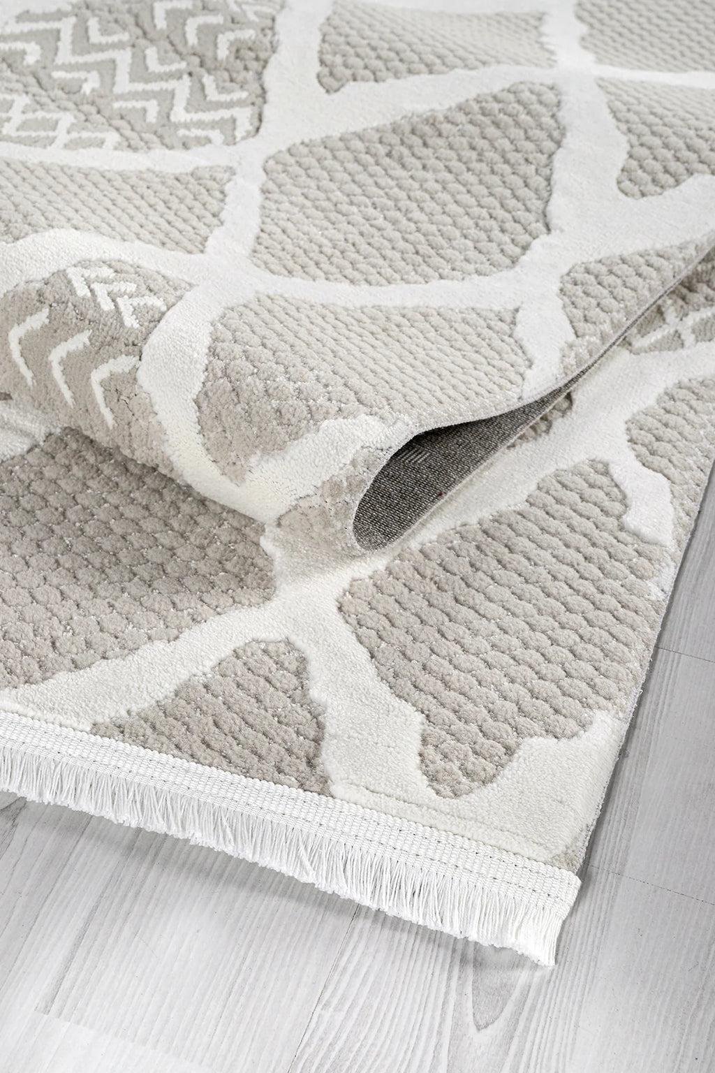 Bej ve beyaz desenli yumuşak dokulu salon halısı, gri parke zemin üzerinde kıvrılmış