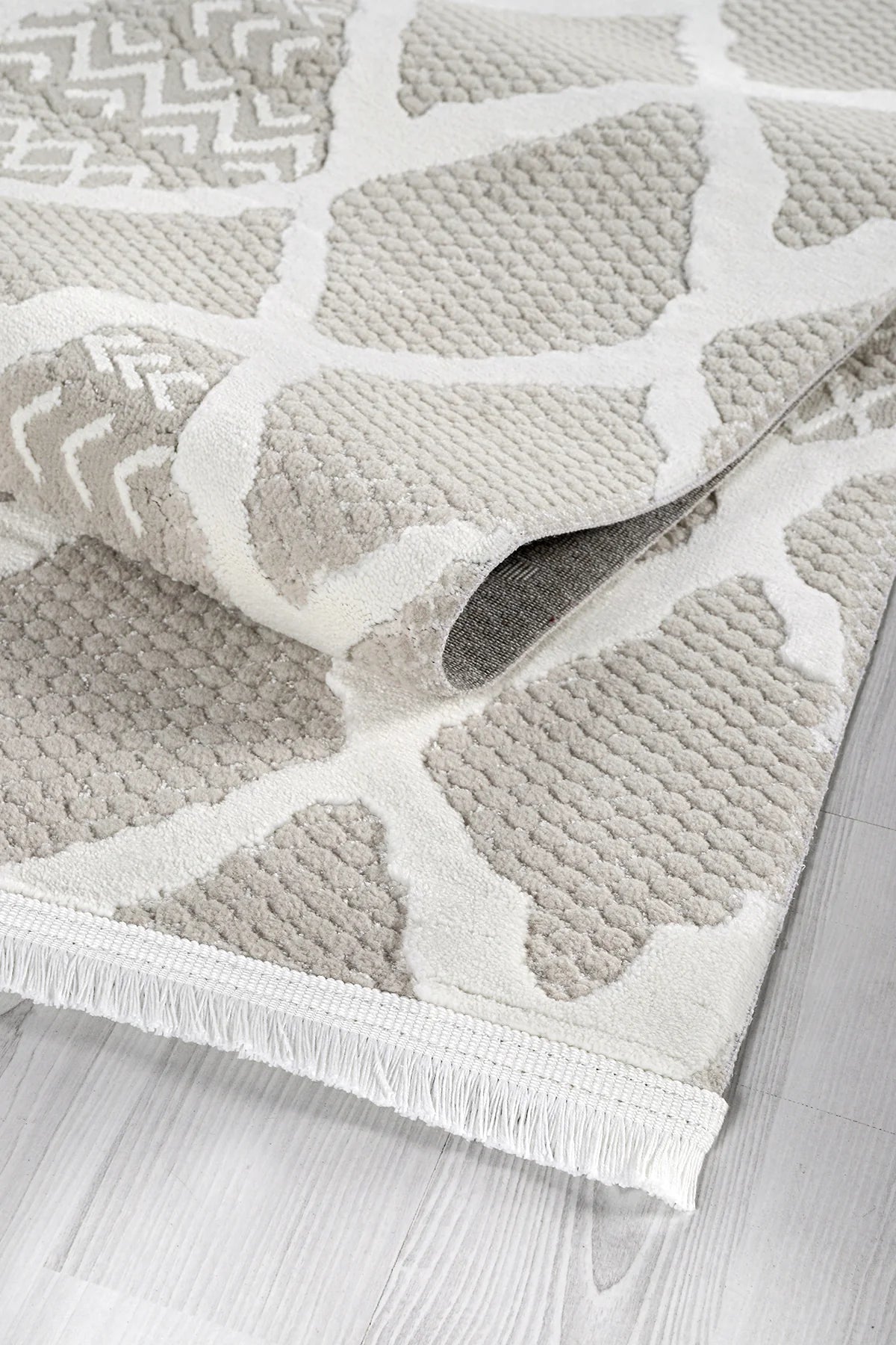 Bej ve beyaz desenli yumuşak dokulu salon halısı, gri parke zemin üzerinde kıvrılmış