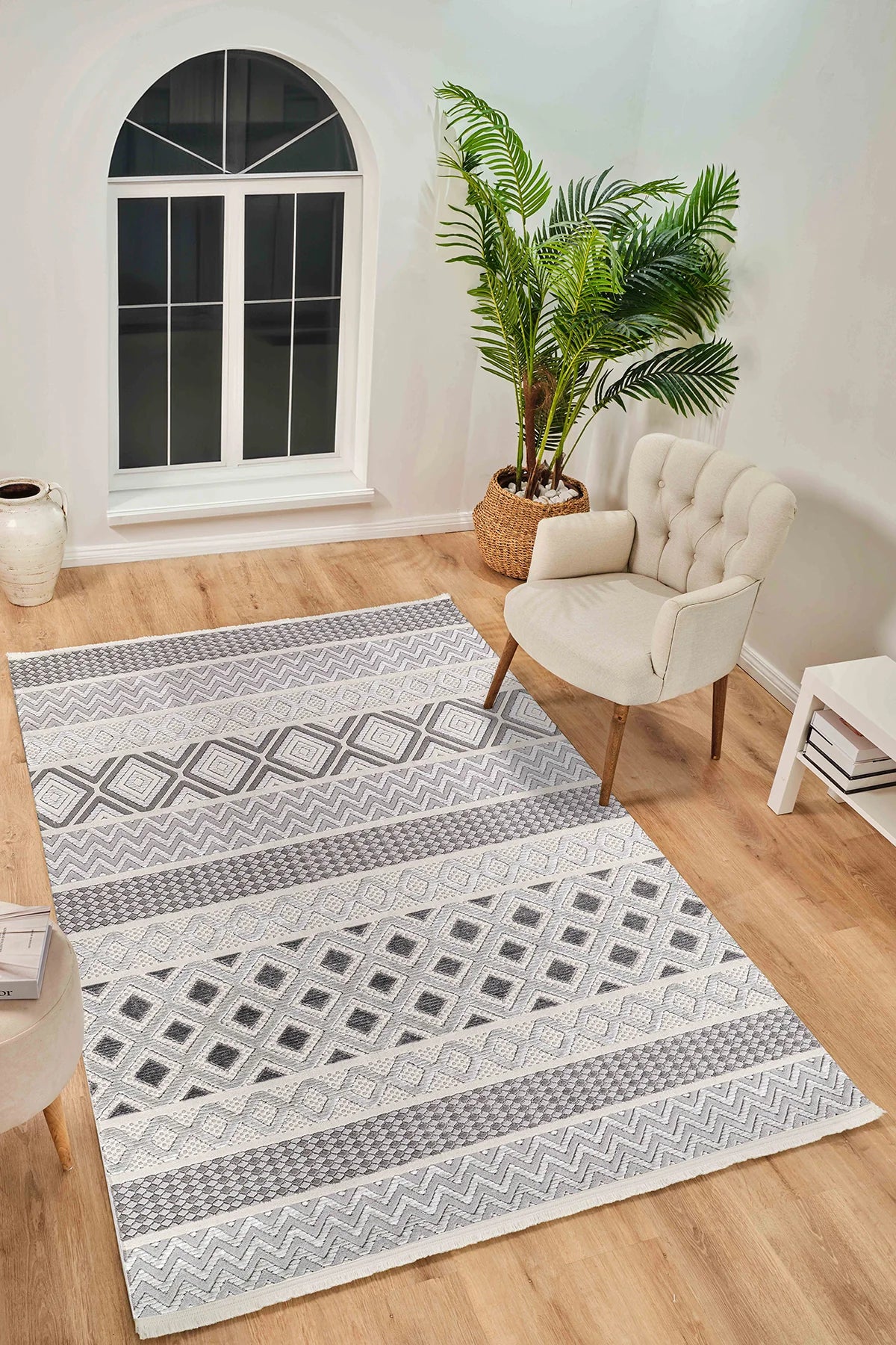 Gri ve beyaz renkli geometrik desenli salon halısı, krem koltuk ve saksıda yeşil bitki