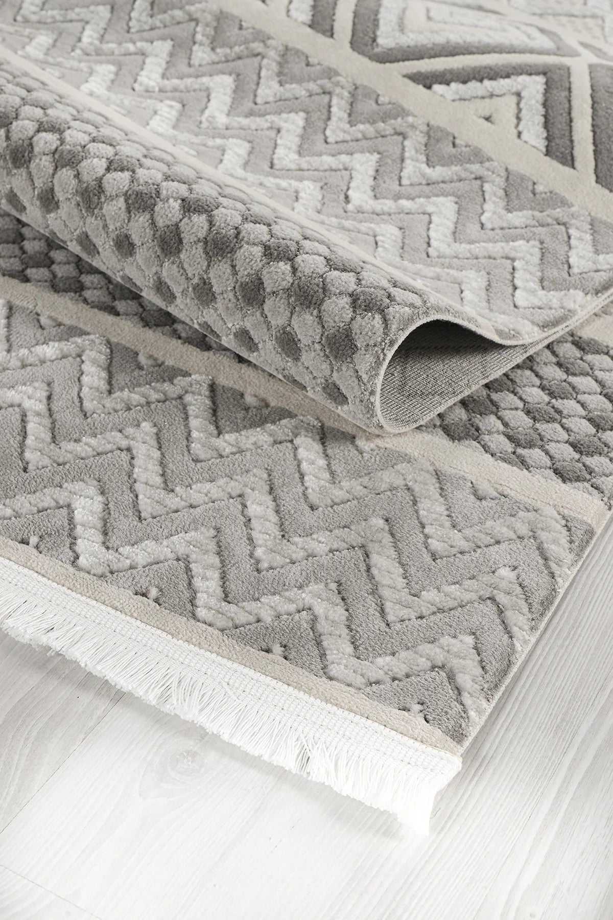 Gri tonlarında dokulu zigzag ve petek desenli makine halısı, beyaz püsküllü kenar