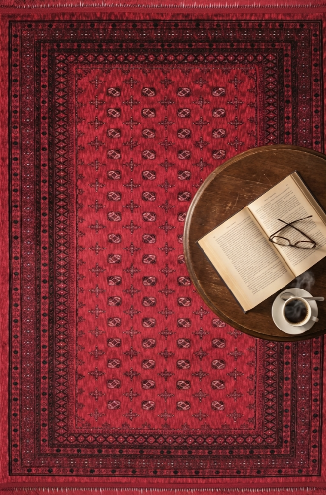 Bordo desenli saten Afgan halısı üzerinde kahve fincanı, açık kitap ve gözlük yer alan yuvarlak ahşap masa