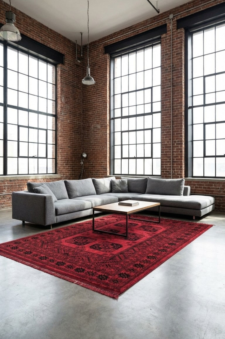 Endüstriyel loft stilde büyük pencere önünde gri köşe kanepe ve üzerine kitap konmuş ahşap sehpa, kırmızı Afgan halı