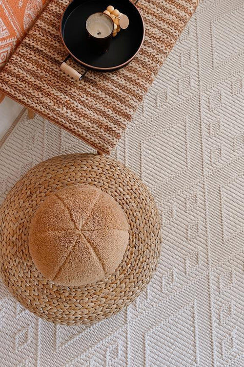 Ekru makine halısı üzerinde dokuma hasır oturma minderi ve kahverengi çizgili minder, siyah tepsi ve mum