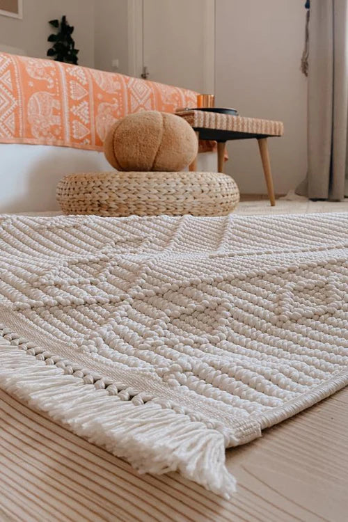 Ekru renkte dokuma makine halısı, odada hasır minder ve turuncu desenli koltuk örtüsü