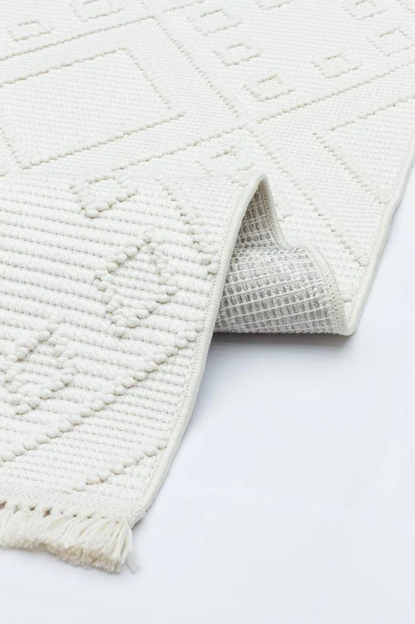 Krem renkte, kabartmalı geometrik desenli makine halısı, detaylı dokuma ve püsküllü kenar