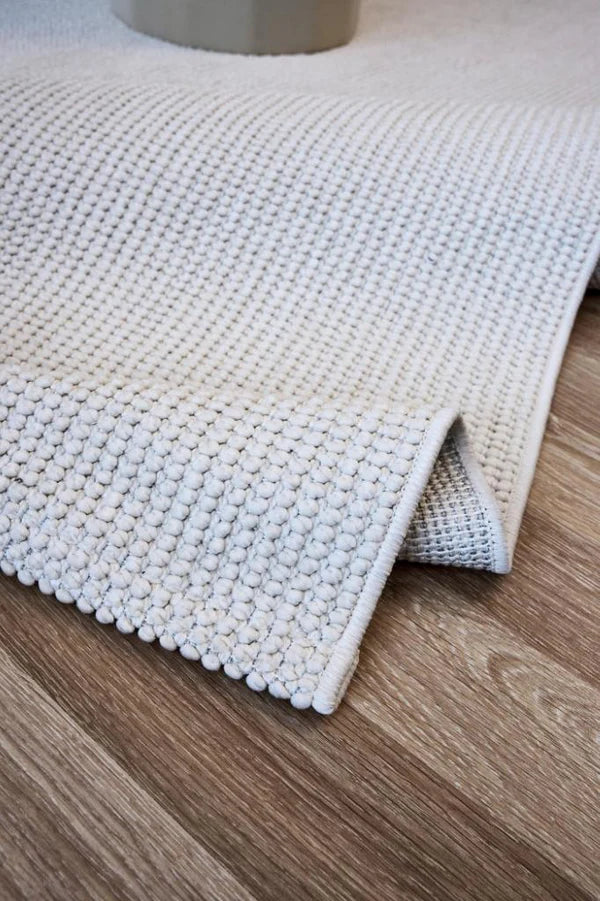 Ekru renkte, dokuma desenli makine halısı, ahşap zeminde serili detay görünümü