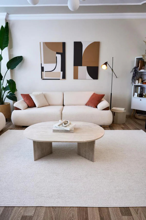 Modern beyaz kanepe, turuncu ve beyaz yastıklar, bej halı, soyut duvar tabloları ve yer lambası