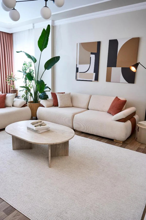 Modern beyaz makine halısı, krem rengi rahat koltuklar, kahverengi yastıklar ve minimalist oturma odası dekoru