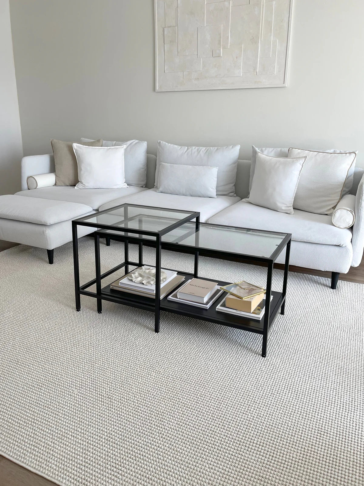 Ekru dokulu makine halısı üzerinde siyah metal cam sehpa ve beyaz büyük köşe koltuk