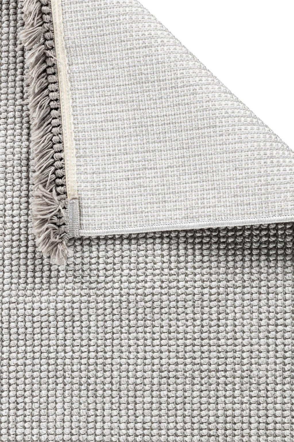 Gri tonlarda desenli makine halısı ve köşesi kıvrılmış, püsküllü kenar detaylı halı