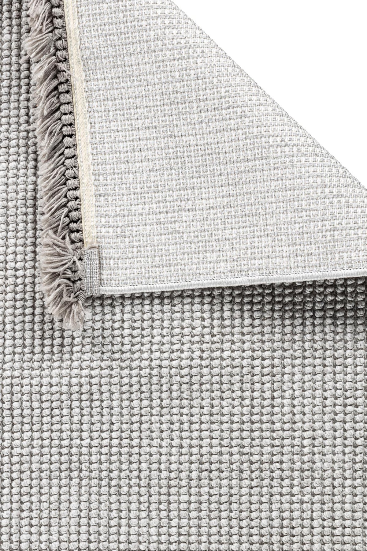 Gri tonlarda desenli makine halısı ve köşesi kıvrılmış, püsküllü kenar detaylı halı