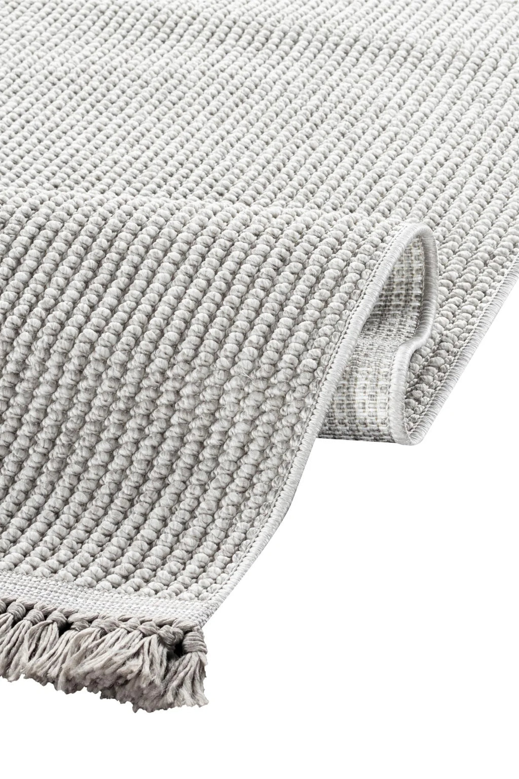 Hafif gri renkli makina halısı, kalın örgü dokusu ve püsküllü kenarıyla