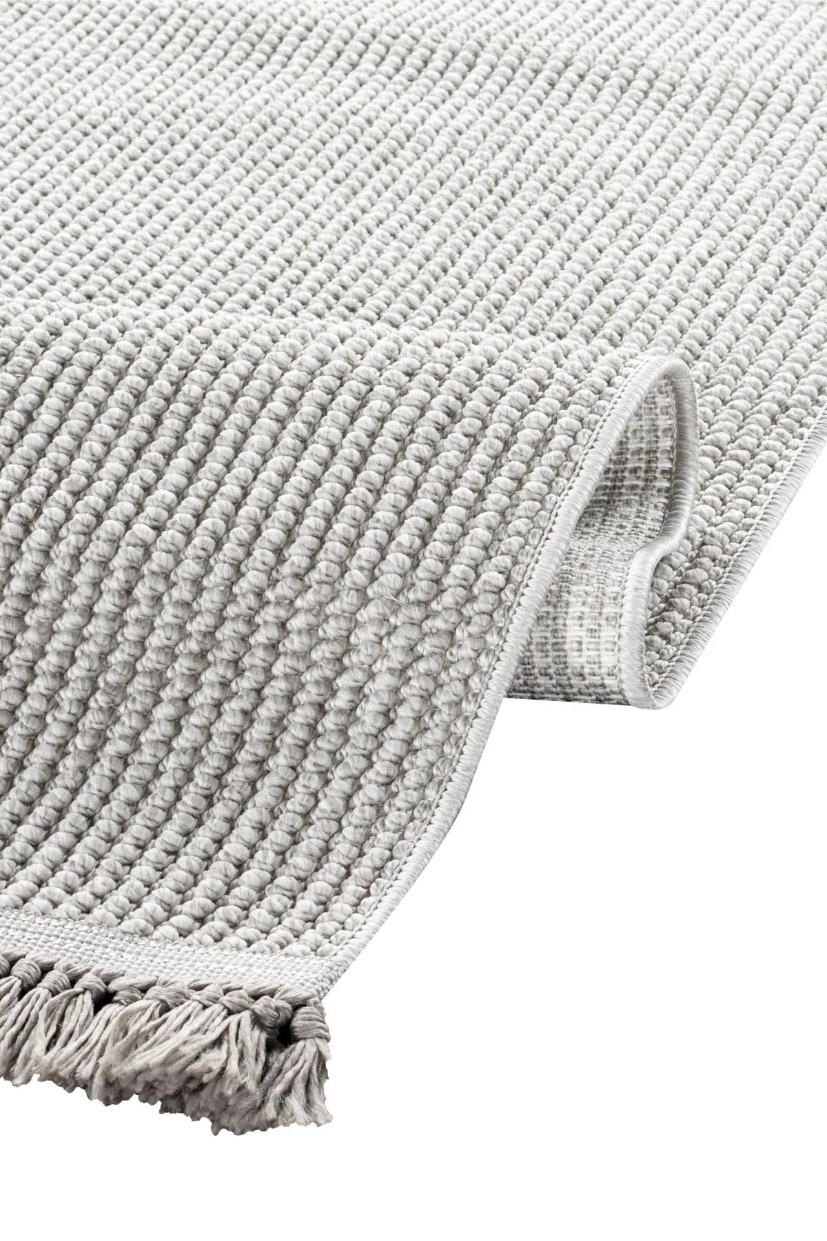 Hafif gri renkli makina halısı, kalın örgü dokusu ve püsküllü kenarıyla
