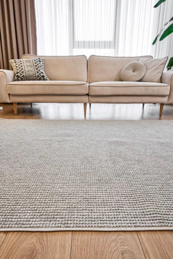 Gri renkli dokuma makine halısı, modern yaşam odasında bej koltuk ve dekoratif yastıklarla