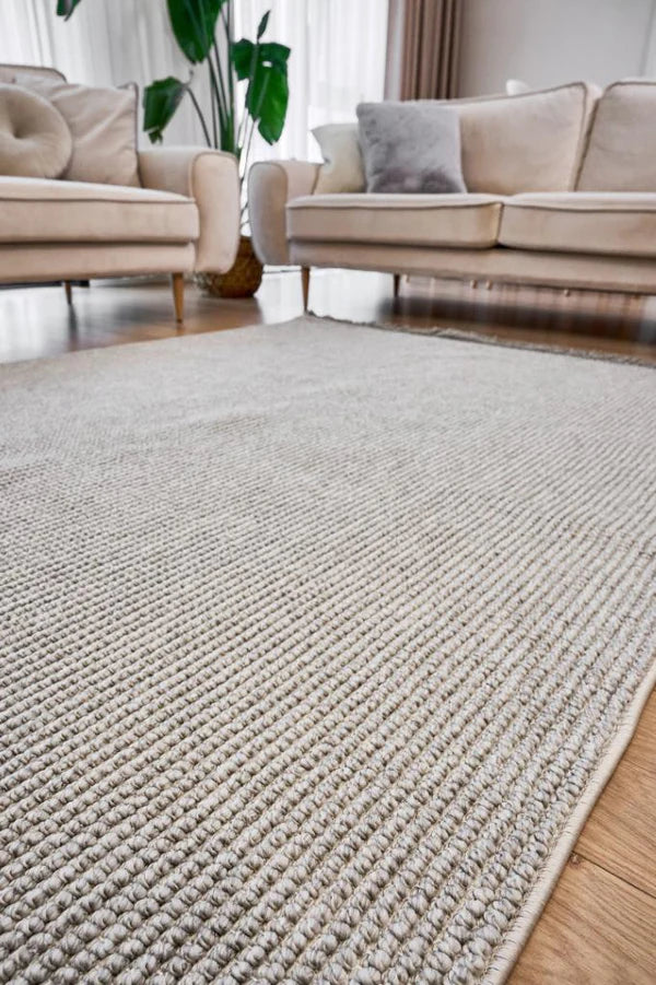 Modern oturma odasında gri makine halısı, bej koltuklar ve bitki dekoru ile