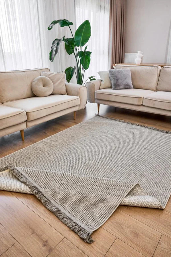 Açık gri makine halısı, modern bej koltuklar ve yeşil salon bitkisi ile şık oturma odası