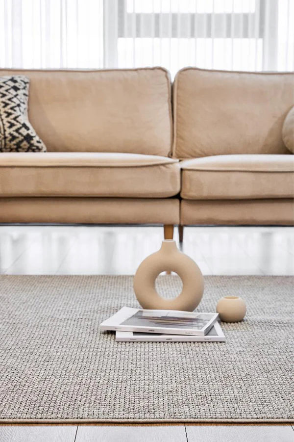 Açık gri dokuma makine halısı üzerinde beige dekoratif obje, kitaplar ve bej koltuk arka planda