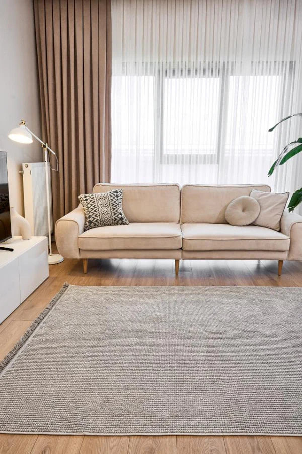 Bej kanepe, siyah beyaz desenli yastık, gri makine halısı ve modern oturma odası dekorasyonu