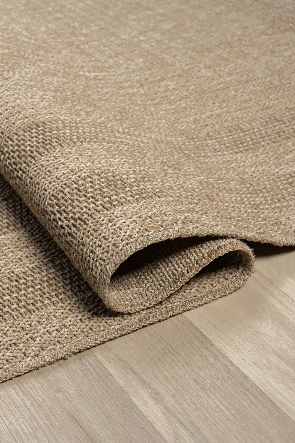 Doğal dokuma bej halı, açık ahşap zeminde kıvrılmış detaylı görünüm