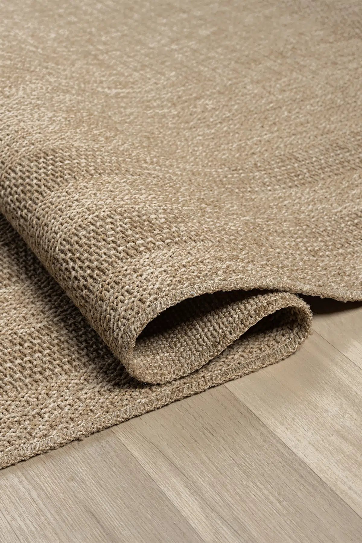 Doğal dokuma bej halı, açık ahşap zeminde kıvrılmış detaylı görünüm