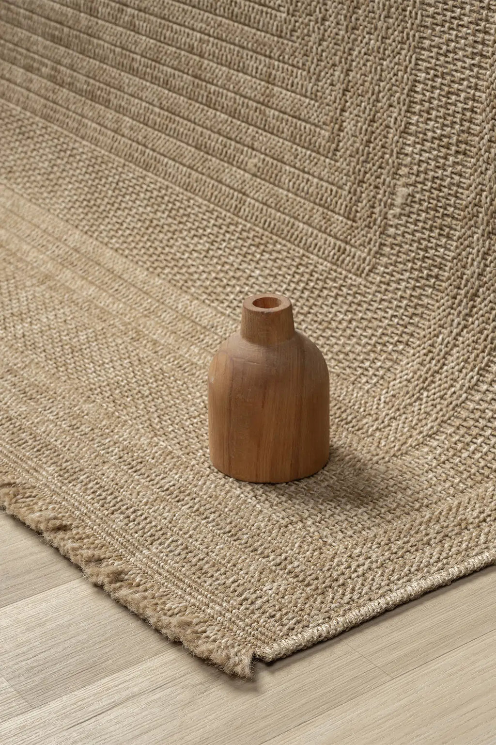 Ön planda doğal dokuma keten halı üzerinde küçük kahverengi ahşap vazo