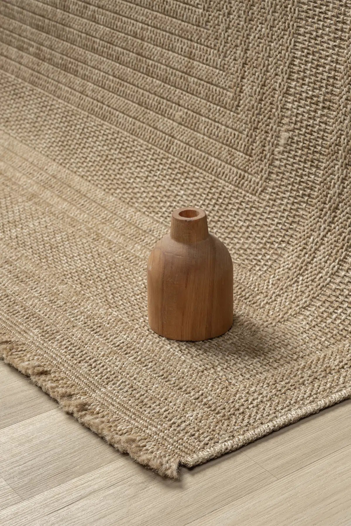 Ön planda doğal dokuma keten halı üzerinde küçük kahverengi ahşap vazo