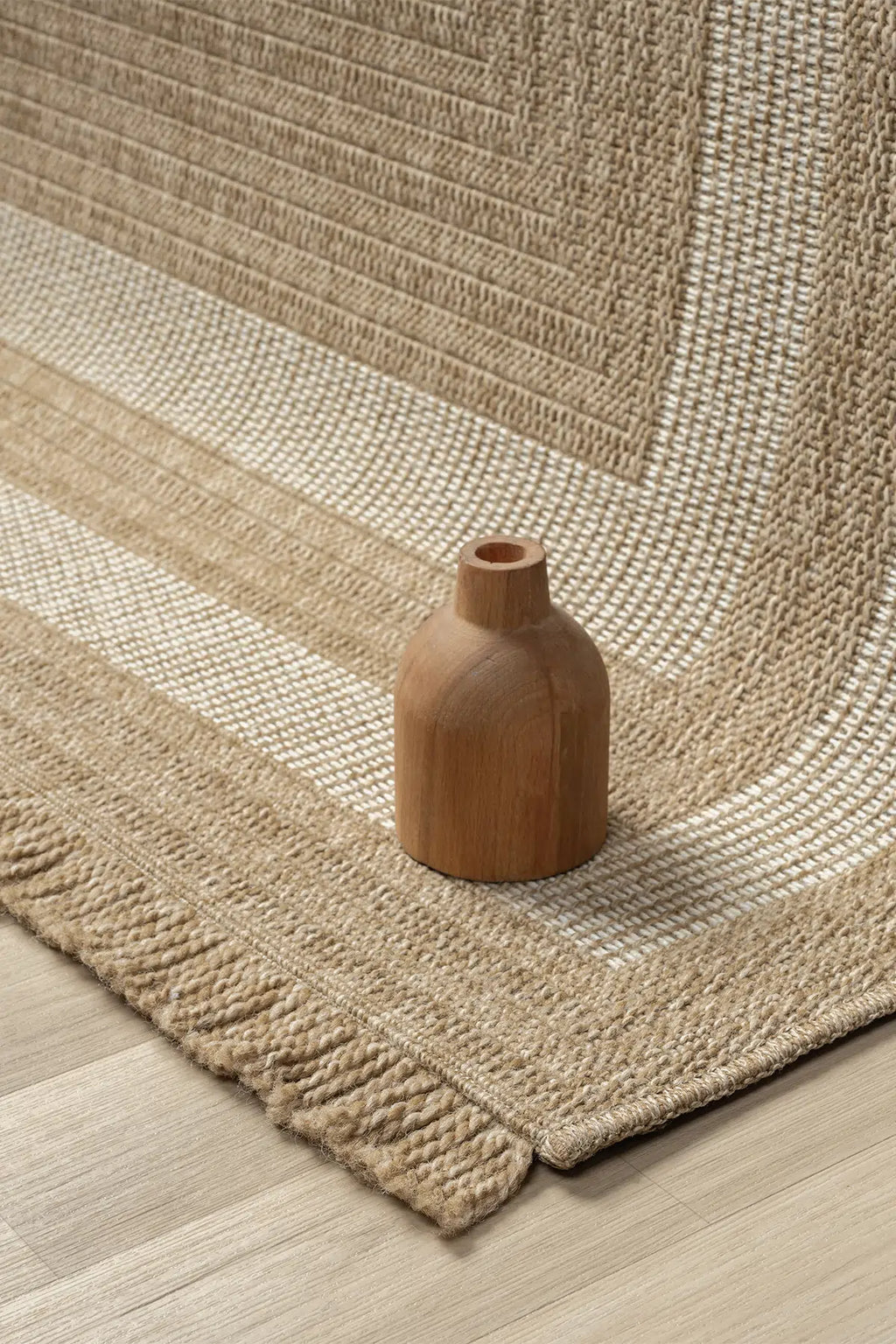 Doğal dokulu bej ve beyaz renkli el yapımı halı üzerinde ahşap vazoya detaylı yakın çekim